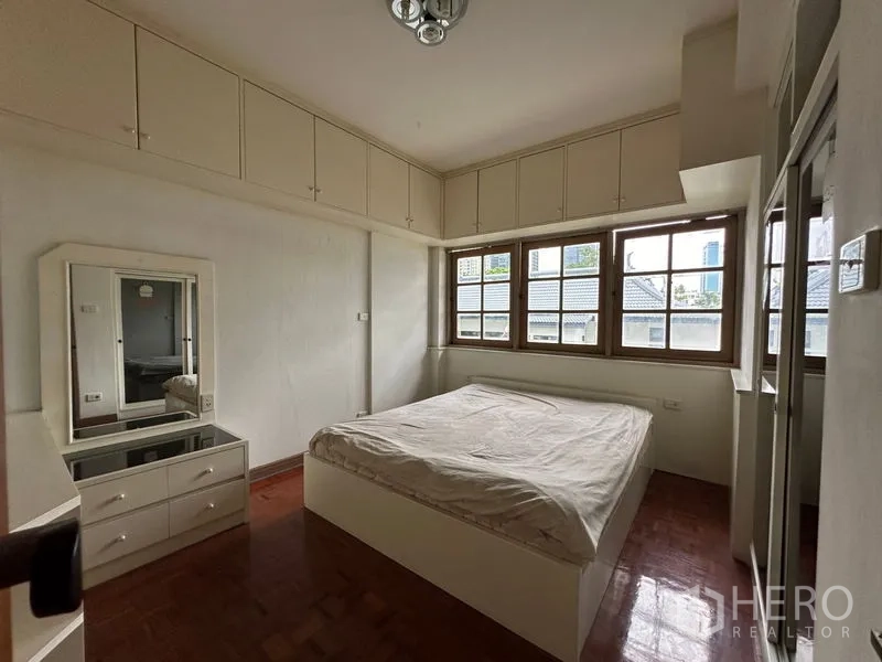 Townhouse for rent in Khlong Toei, Bangkok - Bright bedroom with built-in white cabinetry and large windows.