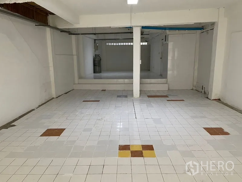 Shophouse for rent in Watthana, Bangkok - Spacious retail area with patterned floor tiles, step-up platform, and exposed ceiling services.
