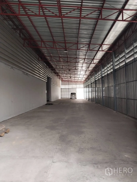Warehouse for rent in Lat Krabang, Bangkok - Long covered loading driveway with metal roof and red steel trusses inside a warehouse complex.