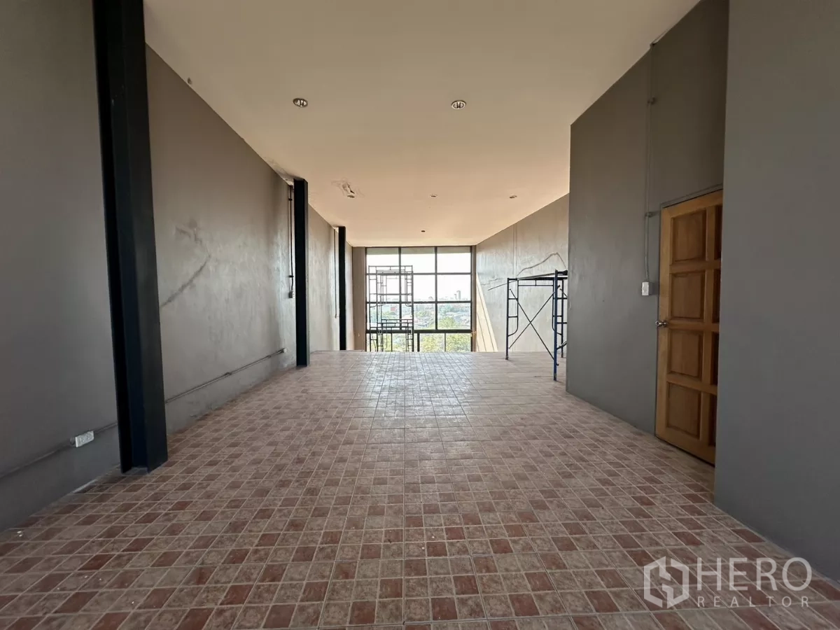 Shophouse for rent in Bang Na, Bangkok - Upper room with tiled floor, steel columns and a full‑height window facing the skyline.