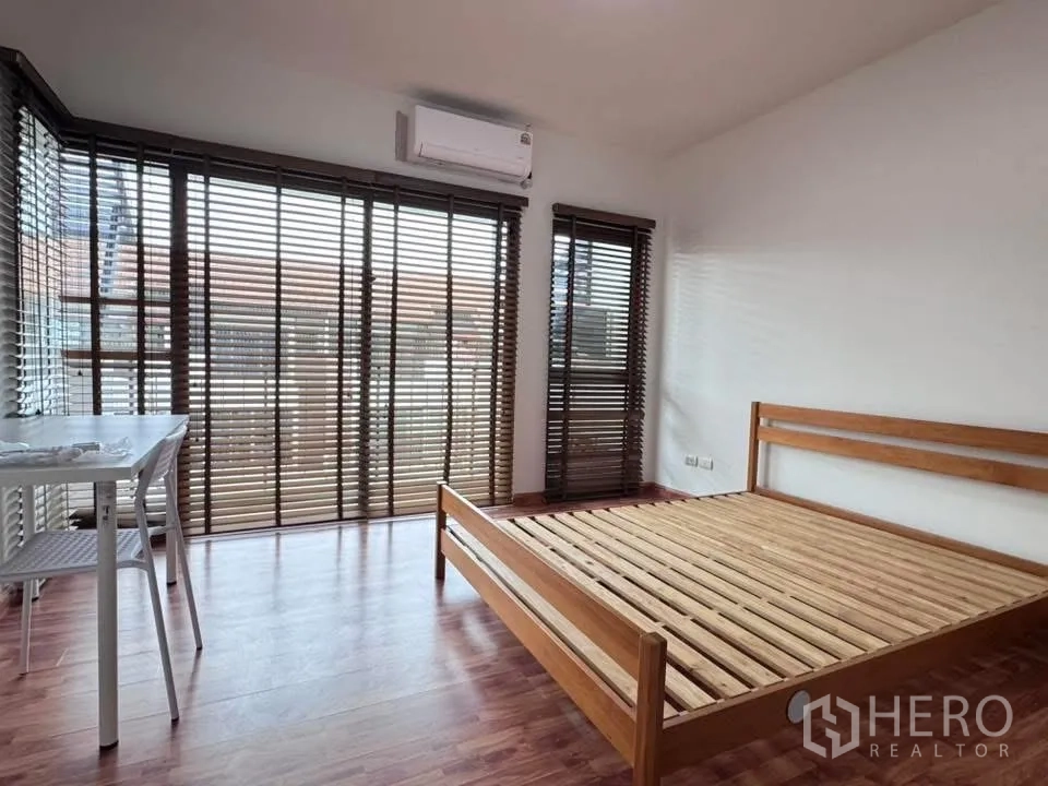 Townhouse for rent in Phra Khanong, Bangkok - Corner bedroom with large windows, wooden bed frame, and blinds.