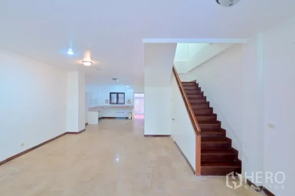 Townhouse for sale in Watthana, Bangkok - Open-plan ground floor with light tile flooring and a wooden staircase leading to upper levels.