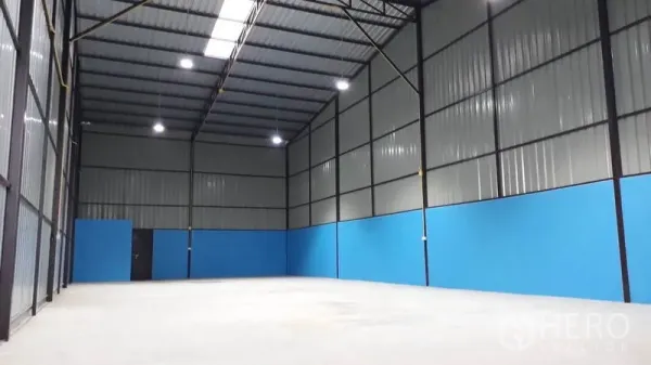 Factory for rent in Khlong Luang, Pathum Thani - Open warehouse-style production space with tall walls, steel trusses and blue lower wall panels.