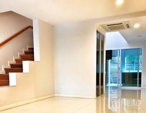 Townhouse for rent in Watthana, Bangkok - Bright living area with white tile floors and a wooden staircase.
