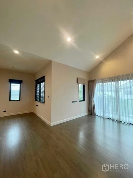 Detached House for sale in Bang Kruai, Nonthaburi - Spacious master bedroom with high sloped ceiling, wood floors and wide windows leading to a balcony.