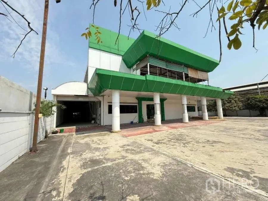 Warehouse for rent in Mueang Samut Prakan, Samut Prakan - Front view of green-and-white office building with wide concrete yard and parking area.