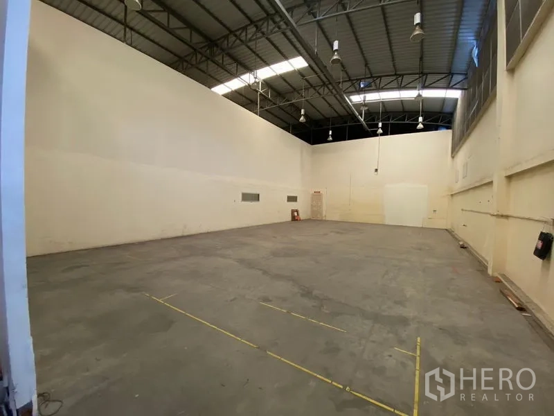 Warehouse for rent in Bueng Kum, Bangkok - Empty storage bay with smooth concrete floor, tall walls and suspended industrial lighting.