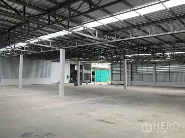 Warehouse for rent in Mueang Pathum Thani, Pathum Thani - Open-plan storage space with high ceiling, concrete flooring and large roller doors for loading.