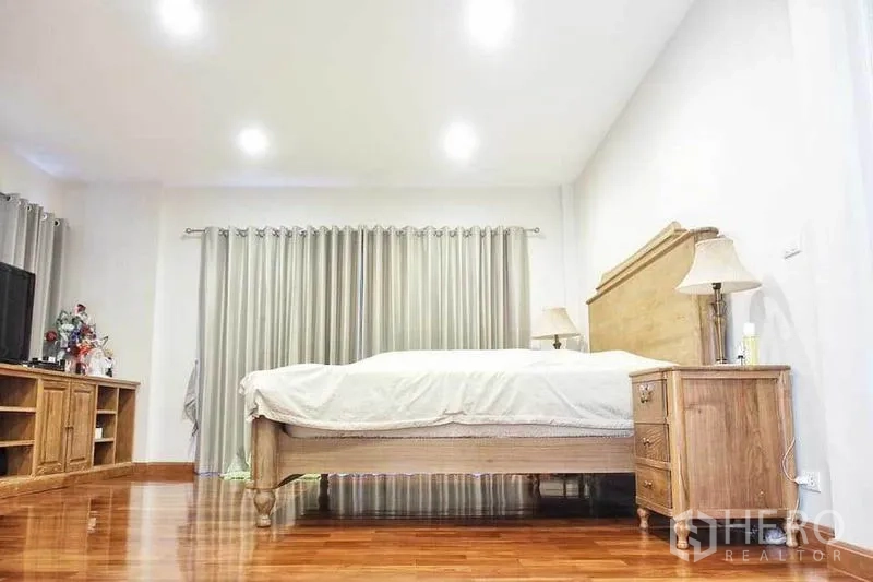 Detached House for rent or sale in Pak Kret, Nonthaburi - Spacious master bedroom with wooden bed, bedside tables, wood flooring and recessed lighting.
