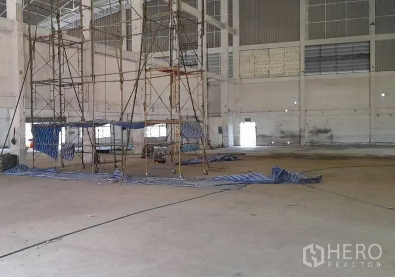 Factory for rent in Mueang Samut Prakan, Samut Prakan - Scaffolding frames and tarps on a concrete floor inside a large manufacturing space.
