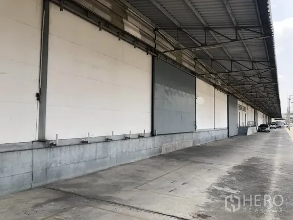 Warehouse for rent in Khlong Luang, Pathum Thani - Covered loading dock with wide roller doors and ample truck maneuvering space along the warehouse facade.
