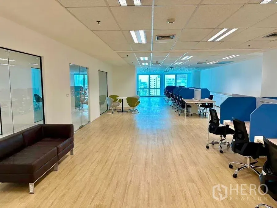 Office Space for rent - Spacious office floor featuring blue-partition desks, a glass-walled meeting room, sofa lounge and bright window light.