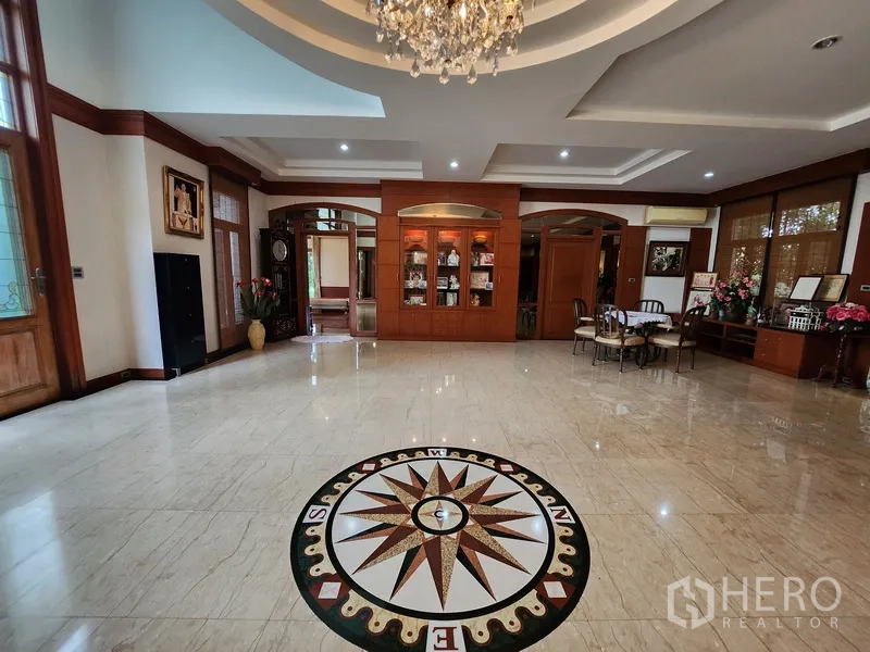 Detached House for rent in Prawet, Bangkok - Grand foyer with marble floor and compass medallion, built‑in wooden cabinetry and chandelier lighting.