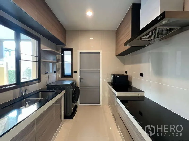 Detached House for rent in Bang Kapi, Bangkok - Fully fitted galley kitchen with windows, black countertops and range hood.