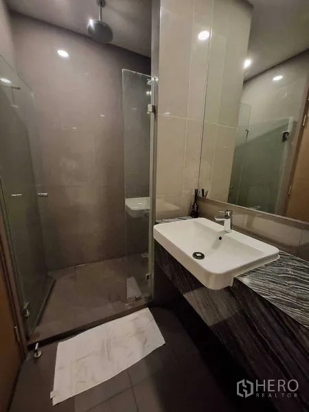Condominium for rent in Bang Rak, Bangkok - Bathroom with glass-enclosed rain shower and long vanity.