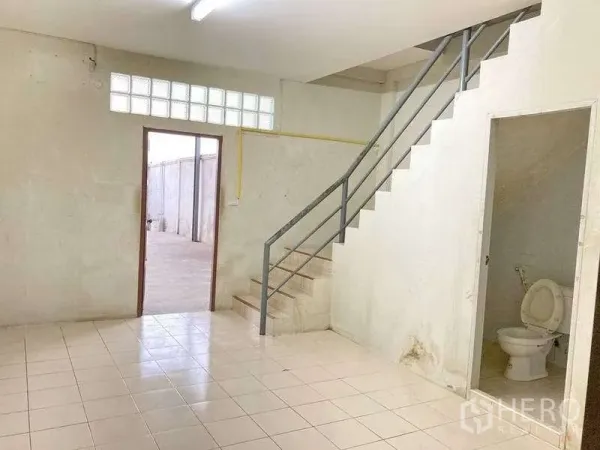 Factory for rent in Samut Prakan - Office area with tiled floor, staircase to a mezzanine and a ground-floor restroom.