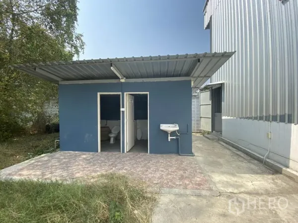Warehouse for rent in Prawet, Bangkok - Separate blue restroom block beside the warehouse with two toilet rooms and an outdoor sink.