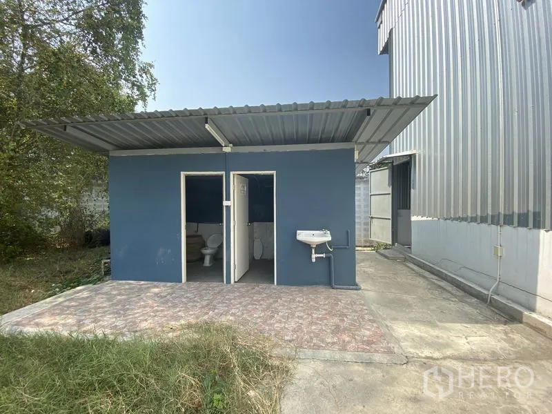 Warehouse for rent in Prawet, Bangkok - Separate blue restroom block beside the warehouse with two toilet rooms and an outdoor sink.