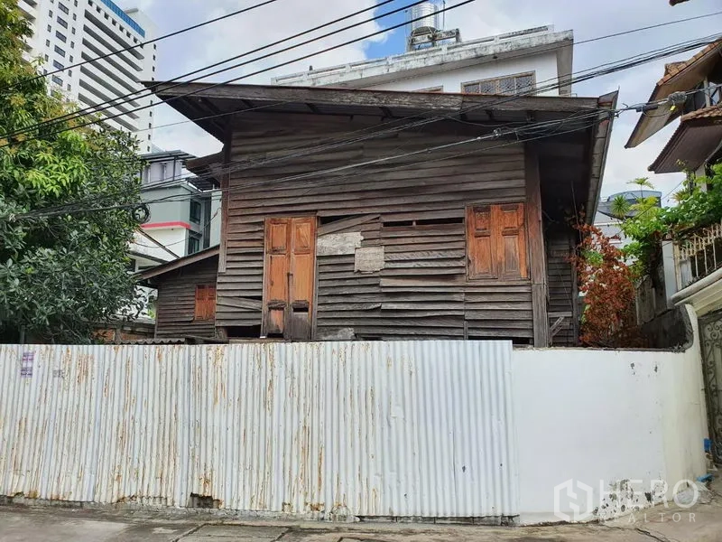Detached House for rent in Sathon, Bangkok - Street view of an aged wooden house behind a white corrugated fence in urban Bangkok.