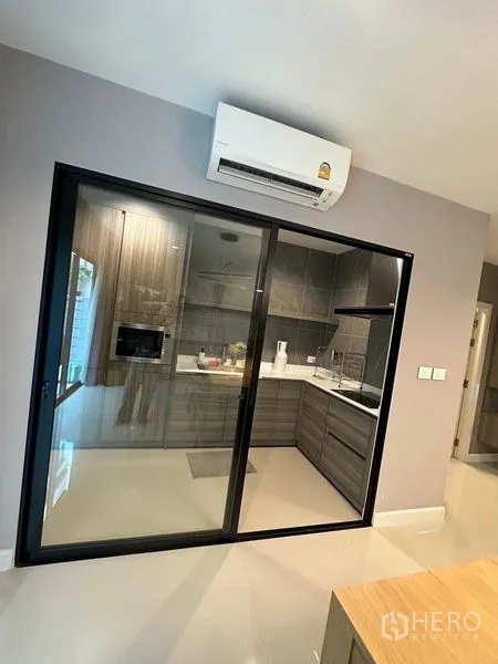 Townhouse for sale in Saphan Sung, Bangkok - Enclosed L‑shaped kitchen behind glass sliding doors with built‑in cabinets and range hood.