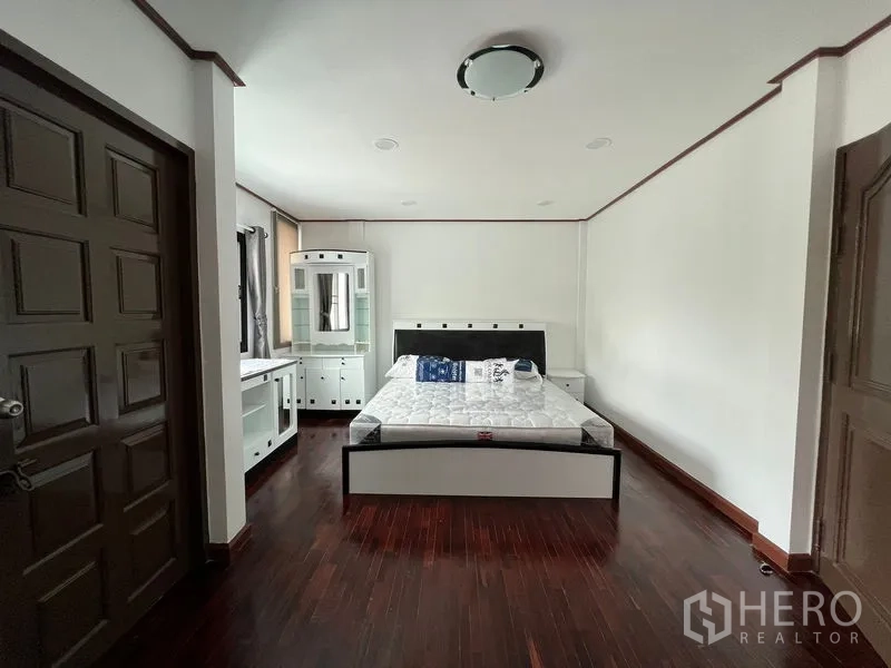 Townhouse for rent in Din Daeng, Bangkok - Spacious master bedroom with bed, vanity unit and polished wood floors.