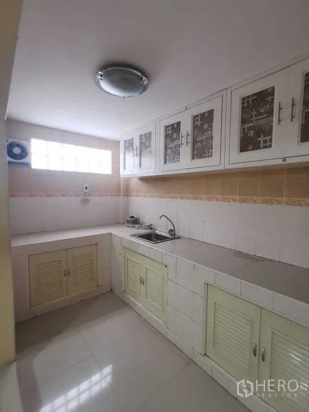Shophouse for rent in Suan Luang, Bangkok - Thai kitchen with white upper cabinets, sink and tiled backsplash.