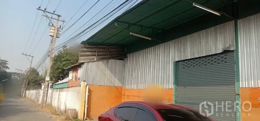 Warehouse for rent in Bueng Kum, Bangkok - Street-side warehouse exterior with corrugated metal cladding, green awning and a large roll-up door in Bueng Kum, Bangkok.