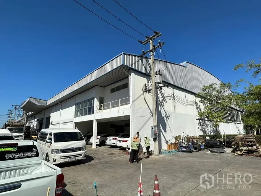 Factory for rent in Si Racha, Chon Buri - Corner view of a modern white factory with metal roof, exterior parking and utility poles under a clear sky in Si Racha.