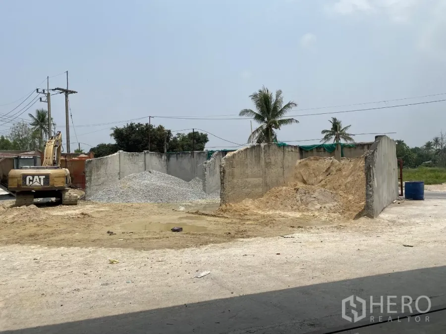 Factory for sale in Chon Buri - Open yard area with excavator, sand and gravel storage bins and palm-lined surroundings inside the factory compound.