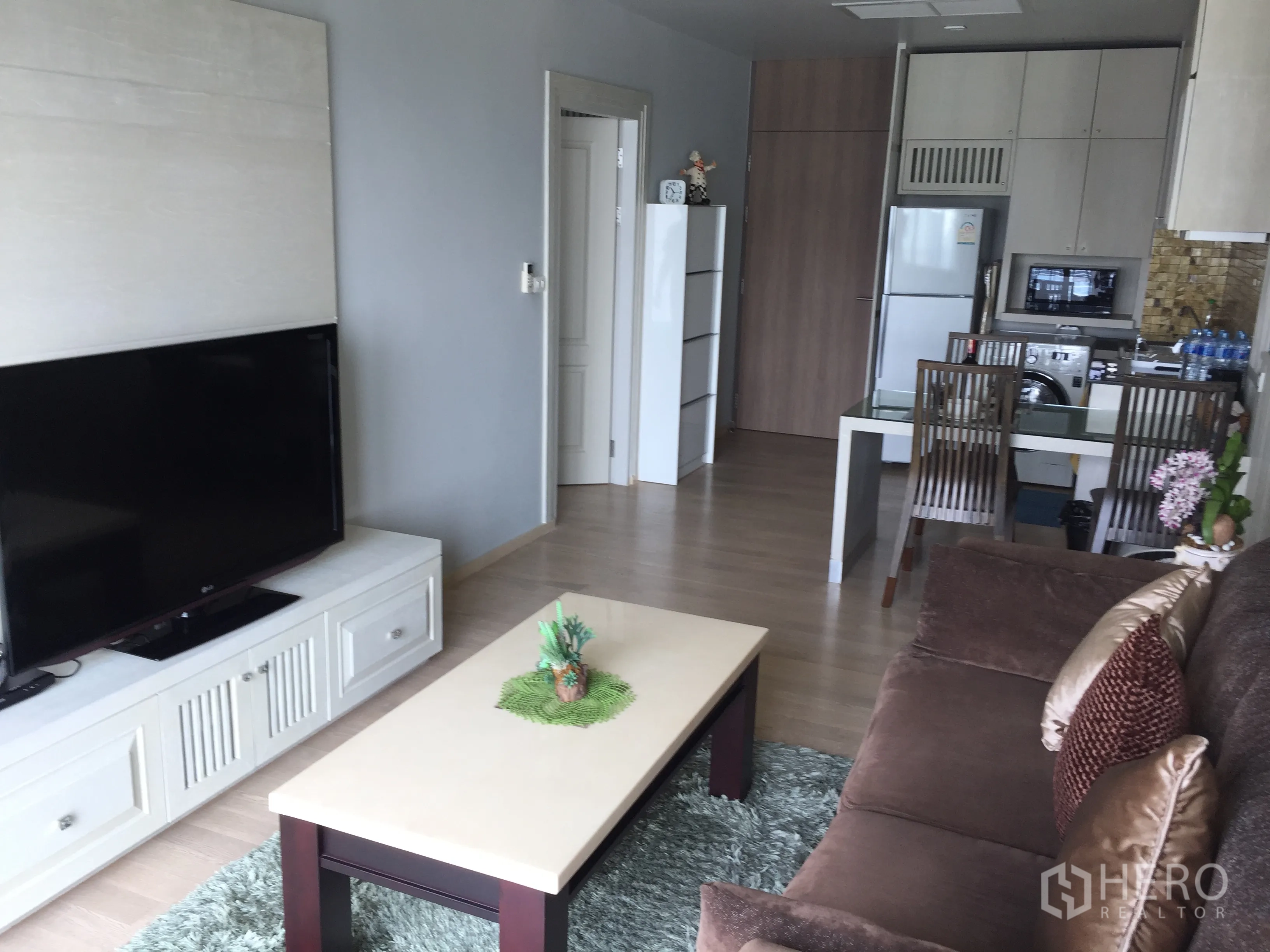 Condominium for rent in Bangkok - Bright living room with large TV, brown sofa, coffee table and open-plan kitchen-dining.