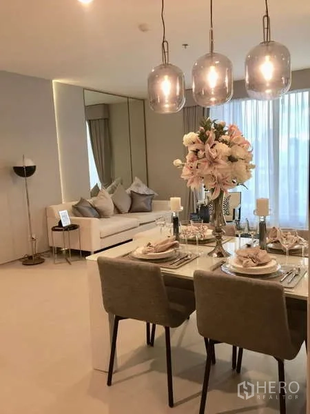 Condominium for rent in Khlong Toei, Bangkok - Dining and living space view showing table for four, sofa and bright windows.