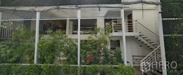 Retail Space for rent in Khlong Toei, Bangkok - Two-level retail space with mezzanine, exterior staircase, and lush green facade.