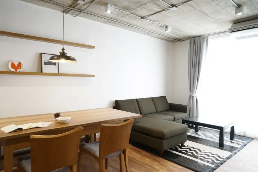 Condominium for rent in Watthana, Bangkok - Bright living and dining area with L-shaped sofa, wooden table, pendant light and full-height curtains.