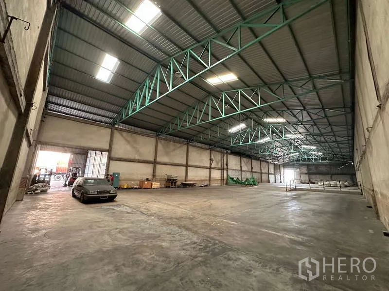 Warehouse for rent in Mueang Pathum Thani, Pathum Thani - Warehouse bay with drive-in access, parked vehicle near loading door and equipment.