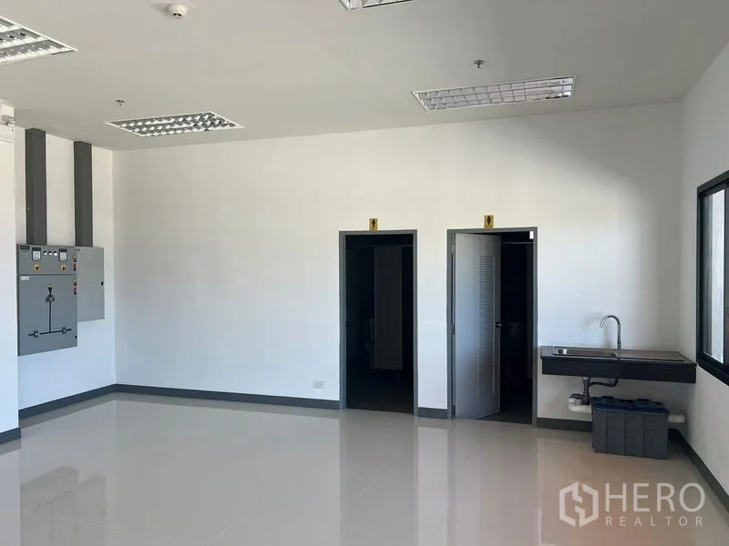 Factory for rent in Bang Pakong, Chachoengsao - Office utility area with electrical panels, two restrooms and a sink by the window.