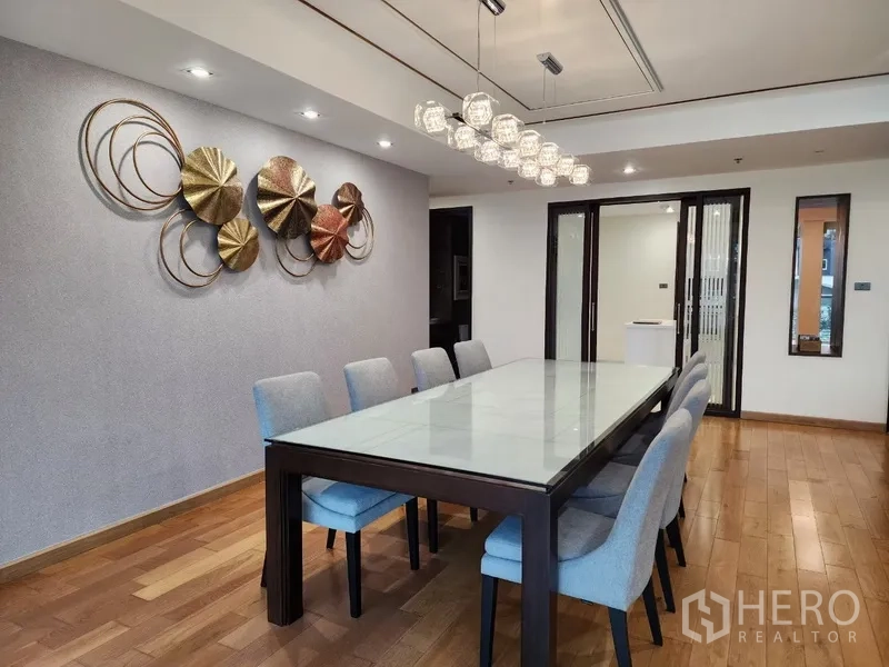 Condominium for rent in Khlong Toei, Bangkok - Eight-seat dining table under crystal pendant lights beside sliding doors.