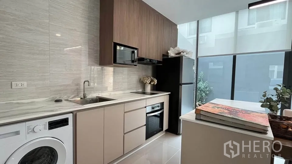 Townhouse for rent or sale in Bang Phli, Samut Prakan - Living area with sofa by large window overlooking garden.