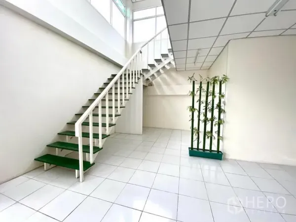 Warehouse for rent in Lam Luk Ka, Pathum Thani - White staircase with green treads leading to a mezzanine office over white tile flooring.
