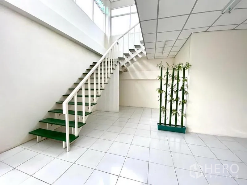 Warehouse for rent in Lam Luk Ka, Pathum Thani - White staircase with green treads leading to a mezzanine office over white tile flooring.