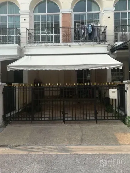 Townhouse for sale in Bang Kapi, Bangkok - Front facade with black metal gate and covered carport awning beneath arched upper windows.