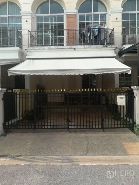 Townhouse for sale in Bang Kapi, Bangkok - Front facade with black metal gate and covered carport awning beneath arched upper windows.