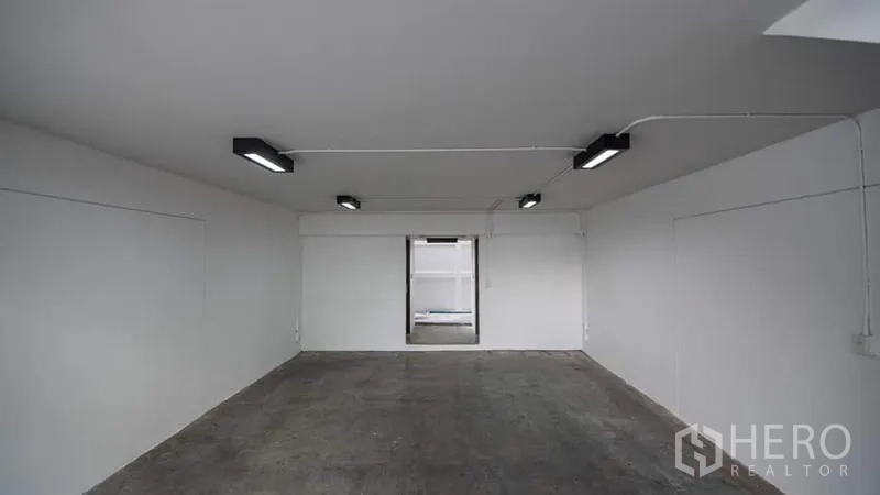 Townhouse for rent or sale in Phra Khanong, Bangkok - Empty indoor garage with concrete floor and strip lighting, ideal for multi-car parking or storage.