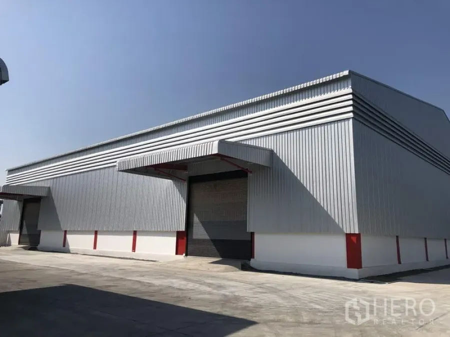 Warehouse for rent in Pak Kret, Nonthaburi - Modern metal-clad warehouse exterior with loading canopy and wide driveway in Pak Kret.