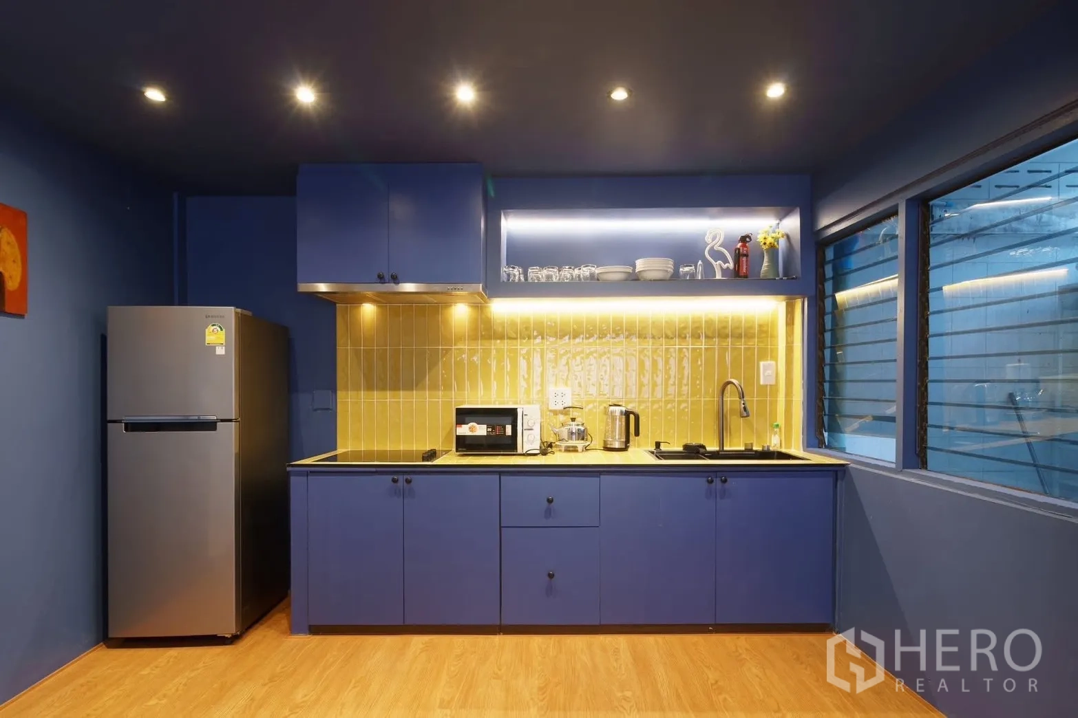 联排别墅 for rent in Watthana, Bangkok - 现代蓝色厨房，黄色背墙，配炉灶、烟机、冰箱与微波炉。