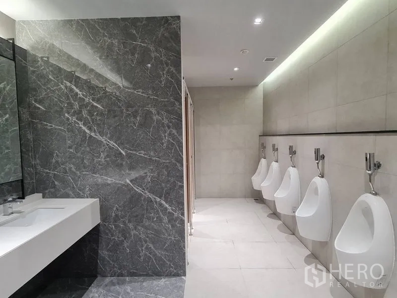 Office Space for rent - Modern men’s restroom with a marble accent wall, long white vanity and a row of urinals in an office building.