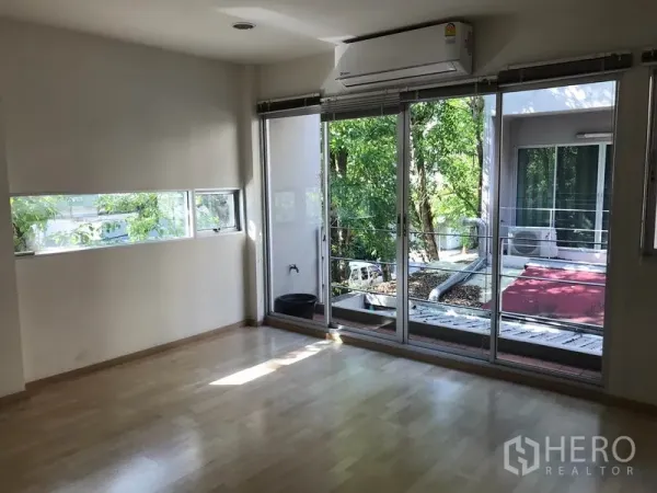 Townhouse for rent in Suan Luang, Bangkok - Bedroom with light wood floors and wide glass doors to a tree-lined balcony.