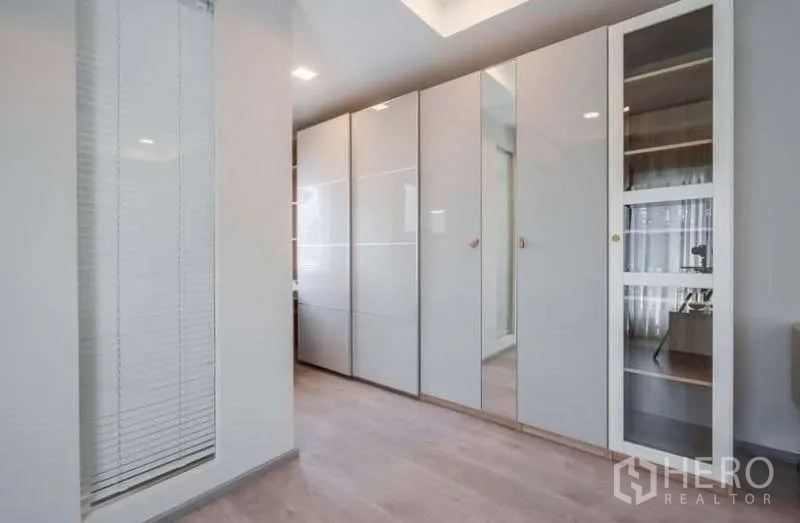 Detached House for rent in Prawet, Bangkok - Walk-in closet corridor featuring glossy floor-to-ceiling wardrobes and light wood flooring.
