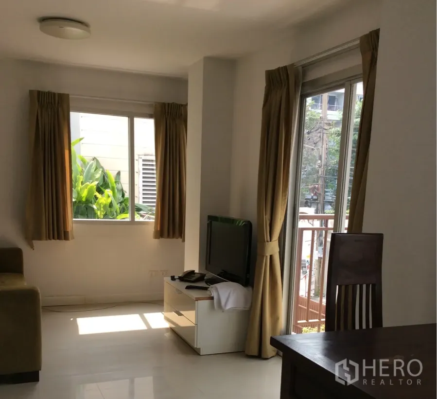 Condominium for sale in Pathum Wan, Bangkok - Bright living room in Pathum Wan condo with TV stand, sofa and balcony doors with beige curtains.