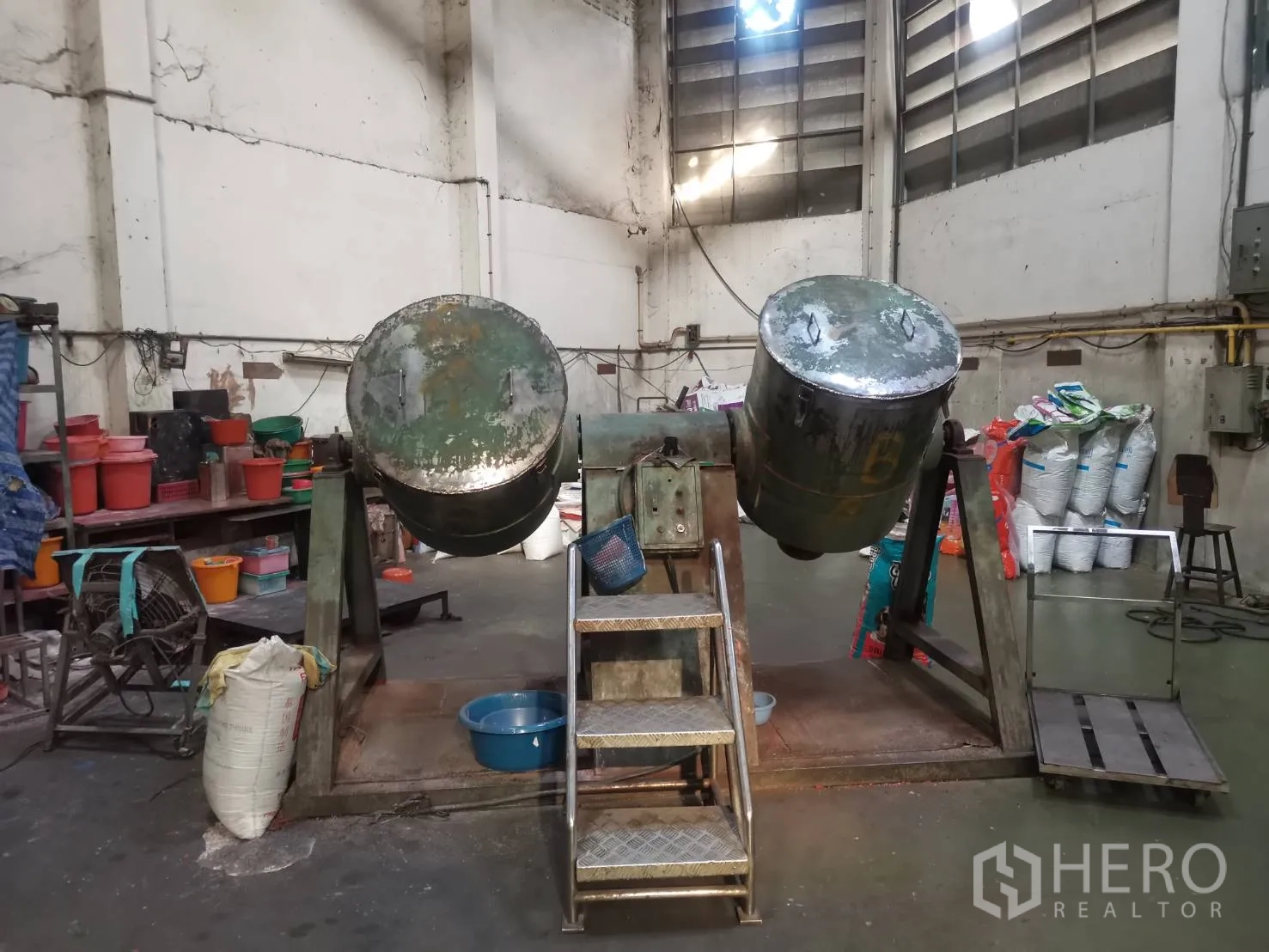 Factory for rent or sale in Bang Khun Thian, Bangkok - Industrial mixing drums mounted on a steel frame with steps in the workshop.