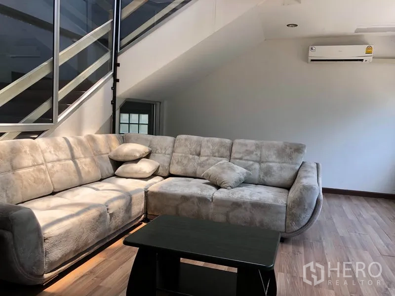 Warehouse for rent in Chatuchak, Bangkok - Cozy upper-floor lounge with sectional sofa beside the stairwell and air conditioner.